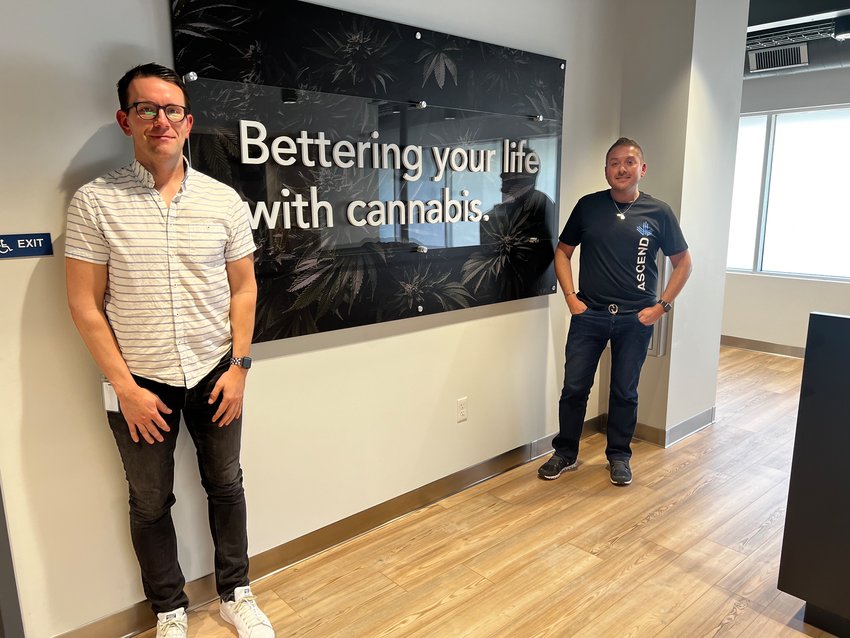 Regional Retail Director Vince Bozman and visiting manager Joaquin Torres stand by a sign at Ascend Cannabis which details its mission statement: “Bettering your life with cannabis.”